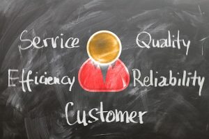 Image is a chalkboard with the words service, quality, efficiency, reliability, and customer written in chalk around the picture of a person.