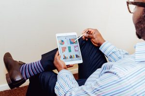 Image is a man holding a tablet with some graphs and pie charts on it.