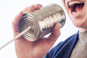 Image is a man talking into a string-and-can play telephone.