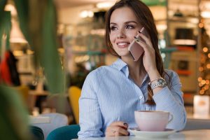 Image is a woman on the phone sitting in a cafe. Image is a woman on the phone sitting in a cafe.
